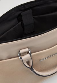 Beige Lederhandtasche mit Reißverschluss, glatter Textur, einem Henkel mit silberfarbener Hardware und einem Innenfutter aus schwarzem Stoff.