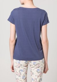 Tmavě modré tričko s krátkými rukávy a kulatým výstřihem, hladké textury a volnějšího střihu, kombinované s květinově vzorovanými světlými kalhotami.
