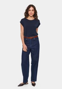 Jūrnieku stila īsās piedurknes tops, apvienots ar augsto vidukli tums zilo džinsu biksēm un brūnu jostu. Modelis valkā melnas slip-on kurpes.