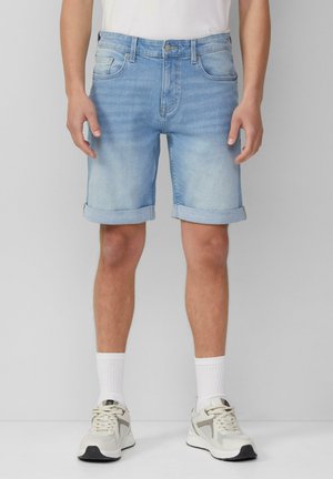 Lichtblauwe denim shorts met opgerolde zoom, vijf pockets en een ritssluiting. Gekozen in combinatie met witte sokken en lichte sneakers.