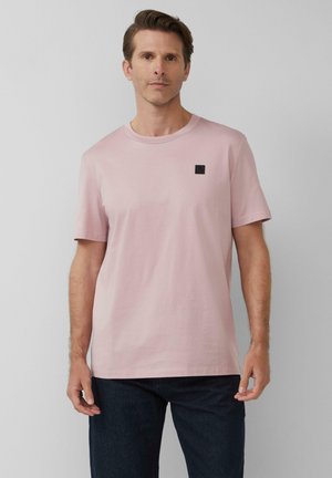 T-shirt rose clair à manches courtes en coton, avec un col rond et une petite étiquette de logo noire sur le haut de la poitrine gauche.