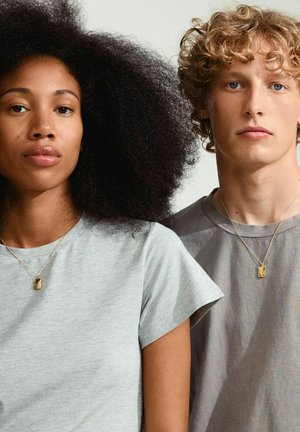 Zwei Personen tragen schlichte Rundhalsausschnitt-T-Shirts: eines in hellgrau mit kurzen Ärmeln, das andere in gedämpftem Grau. Beide tragen goldene Halsketten.