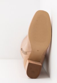 Bottine beige avec fermeture éclair latérale, semelle texturée, talon bloc, et taille 37 imprimée sur la semelle, positionnée semelle vers le haut sur fond blanc.