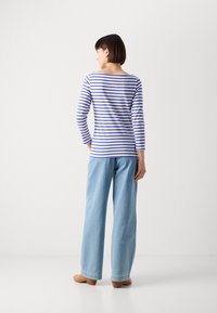 Stripet langermet topp i hvit og blå, sammen med lyseblå vide jeans og beige sko, sett fra baksiden.