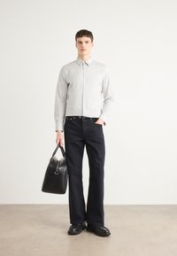 Camisa de botones a rayas gris claro, jeans anchos de mezclilla azul marino, y bolso de cuero negro, combinados con botas de tobillo negras sobre un fondo neutral.