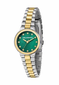 Montre ronde avec un cadran vert, un bracelet métallique bicolore or et argent, des index semblables à des diamants et une lunette texturée. Le nom de la marque est affiché au-dessus du cadran.