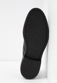 Semelle de chaussure noire avec motif de grip texturé et bords lisses. Comprend un logo de marque en relief et un détail de taille pour identification.