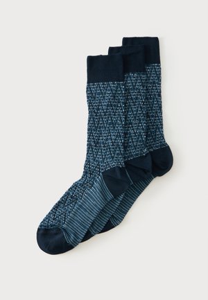 Drie paar donkerblauwe sokken met patroon, met effen navy tenen, hielen en boordjes, overlappend gerangschikt op een lichte achtergrond.