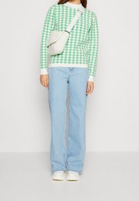 Maglione a quadretti verde e bianco, jeans larghi color blu chiaro e borsa a tracolla crema con texture; sneakers bianche con suola spessa.