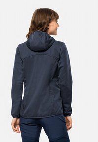Veste softshell navy avec capuche, dotée d'une texture lisse et de poignets élastiques. Le dos présente un design ajusté et des coutures discrètes.