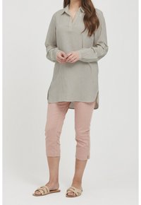 Szara tunika w paski z kołnierzykiem, długimi rękawami i rozcięciami po bokach, zestawiona z różowymi spodniami 7/8. Sandały mają zaprojektowane skręcone paski.