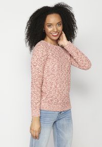 Raudonas ir baltas margintas megztinis su ilgomis rankovėmis ir apvaliu iškirpimu, derinamas su šviesiai mėlynomis džinsais. Kasdienis siluetas, tekstūruotas raštas.