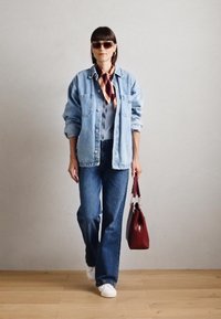 Veste en denim sur une chemise bleu clair, avec un jean bleu et des baskets blanches. Tenue d'un sac bordeaux avec quincaillerie argentée, lunettes de soleil et écharpe.