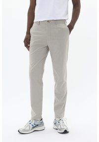 Pantalones beige a medida con pierna recta, textura suave y un solo botón frontal. Combinados con zapatillas grises con acentos azules.