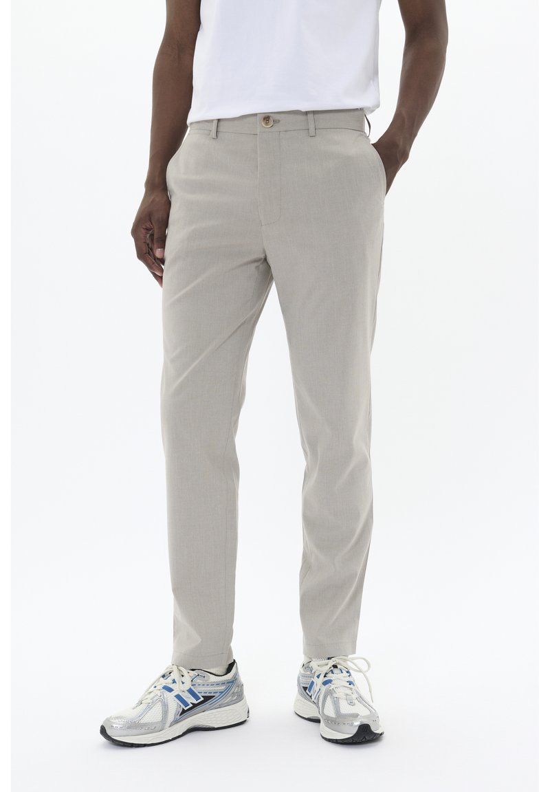 Pantalones beige a medida con pierna recta, textura suave y un solo botón frontal. Combinados con zapatillas grises con acentos azules.