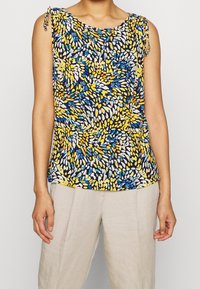 Top sin mangas con un patrón multicolor de formas azules, amarillas y blancas sobre un fondo oscuro; tirantes fruncidos con acentos decorativos.