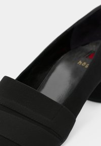 Black flat shoe with a smooth finish, featuring a wide fabric band across the top and a sleek, rounded toe design.