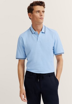 Light blue short-sleeve polo shirt with a three-button placket and navy stripes on the collar and sleeves, paired with dark pants.