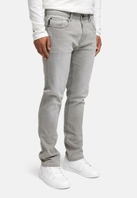 Jeans en denim gris clair avec une coupe droite, dotés de cinq poches et de quincaillerie noire. Associés à des baskets blanches.