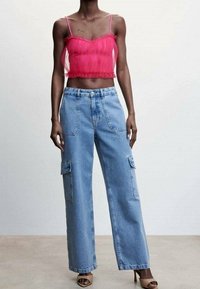 Top corto rojo transparente con dobladillo con volantes, combinado con pantalones cargo de pierna ancha en azul claro que cuentan con bolsillos laterales y un corte relajado. Sandalias de tacón alto.