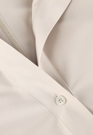 Beige blouse with a smooth texture, featuring a partial button closure and subtle stitching detail along the collar and placket.