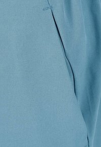 Tejido azul claro con una textura suave, que presenta un sutil detalle de plisado en el costado. El material tiene un acabado mate.