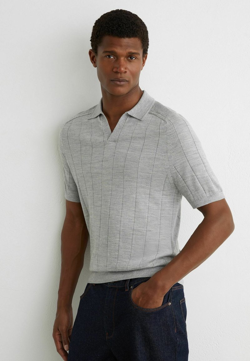 Halli lühikeste varrukatega polo-särk, millel on vertikaalne sooniktekstuur, krae ja v-kaela kujundus. Kandmiseks koos tumel siniste teksapükstega ning näitab vabalt istuvat lõiget.