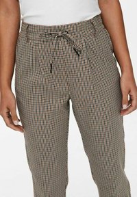 Rutig byxor i tan, brunt och svart med resårmidja och dragsko. Har sidofickor och en avslappnad passform.