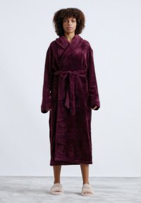 Pehmeä viininpunainen bathrobe, jossa on huppukolari, vyö vyötäröllä ja kaksi etutaskua. Pehmeä pinta ja täydet hihat.