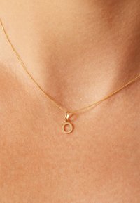 Gouden ketting met een fijne ketting en een ronde hanger met een open ontwerp. Gladde textuur en subtiele glans op de huid.