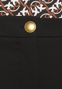 Svarta byxor i tyg med en guldknapp med "PINKO" ingraverat, tillsammans med ett mönstrat midjeband i bruna och vita nyanser.