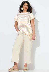 Camiseta a rayas blanca y naranja con borde de encaje, combinada con pantalones de pierna ancha beige y sandalias planas. Modelo sosteniendo un bolso de mano tejido.