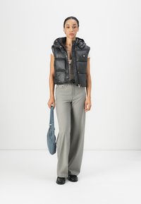 Zwarte gewatteerde vest met een capuchon, ritssluiting aan de voorkant en glanzende textuur; grijze, high-waisted broek; blauwe handtas met een lange schouderband; zwarte schoenen.