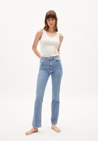 Jeans de tiro alto en un azul claro con un corte recto y detalles de costura mínimos. Combinados con una camiseta sin mangas blanca ajustada.