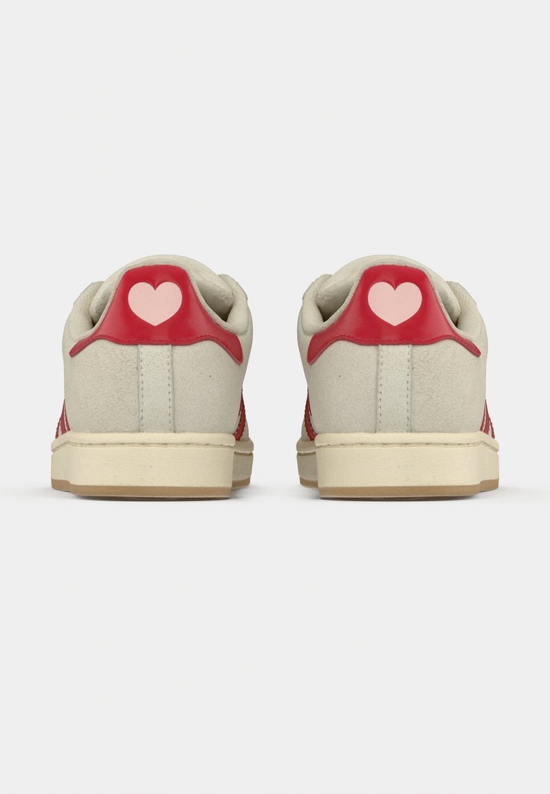 Des baskets rouges et beiges avec une tige texturée, un accent rouge au talon orné d'un cœur rose, et une semelle en caoutchouc.