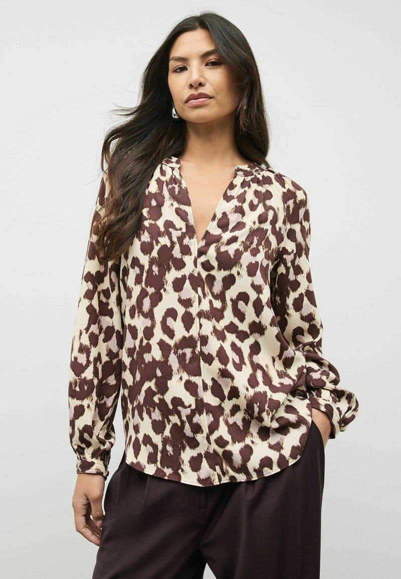 Blus dengan motif macan tutul berwarna beige krim dengan aksen coklat. Memiliki leher V, lengan panjang, dan potongan santai. Tekstur kain yang halus.