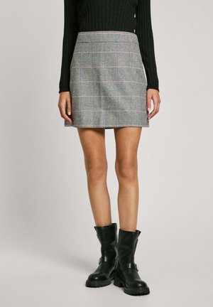 Jupe à carreaux gris avec des accents bleus et rouges, tissu lisse, design ajusté, longueur genou, associée à des bottines en cuir noir.