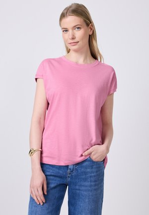 T-shirt rose à manches courtes, col rond, texture douce, coupe décontractée, associé à un jean en denim bleu clair, le modèle porte un bracelet en or au poignet.