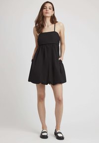 Rompers sans manches noir avec taille froncée, shorts évasés et poches latérales, fabriqué à partir d'un tissu léger. Design minimaliste.