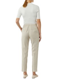 Jasnobeżowe dopasowane spodnie z dwiema kieszeniami z tyłu, w zestawie z dopasowaną białą bluzką z krótkim rękawem. Materiał ma gładką teksturę.