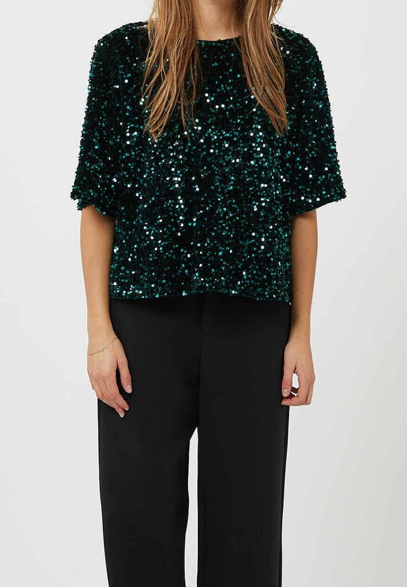 Top in paillettes verde scuro scintillante con una vestibilità ampia, scollatura rotonda e maniche corte, abbinato a pantaloni neri a gamba larga.