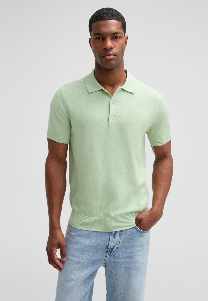 Jasnozielona koszulka polo z krótkim rękawem i żebrowanym dołem oraz kołnierzykiem, posiadająca trzy guziki i miękką teksturę. Połączona z jasnymi dżinsami.