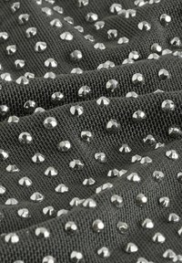 Tessuto con una superficie in morbido grigio scuro decorata da numerosi chiodini argentati, creando un motivo testurizzato e disegnato.