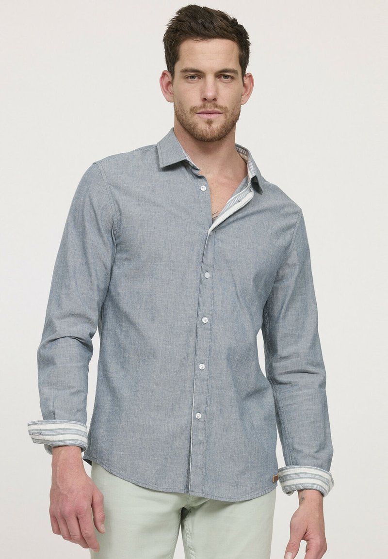 Chemise boutonnée bleu clair en tissu texturé, avec un col et des poignets rayés contrastants. Design ajusté, patte de boutonnage à l'avant.