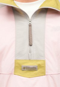 Κοντινό πλάνο ενός pastel ροζ και κίτρινου μπουφάν Columbia Sportswear με εμπρόσθιο φερμουάρ και υφασμάτινη ετικέτα μάρκας.