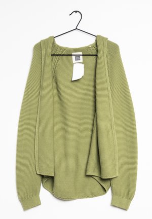 Cardigan tricoté vert clair suspendu sur un cintre noir avec une étiquette de prix blanche attachée à l'intérieur du col sur fond blanc.