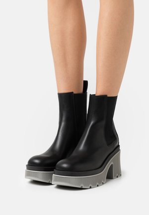 Black leather ankle boots with elastic side panels, featuring a chunky grey ridged sole and a sleek design.