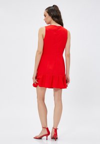 Vestido rojo sin mangas con un dobladillo acampanado, cuerpo ajustado y cremallera en la espalda. Combinado con sandalias rojas de tacón alto. Textura de tela suave.