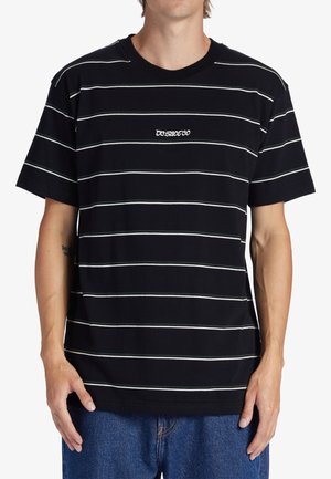 Mann trägt ein schwarzes kurzärmeliges T-Shirt mit dünnen weißen horizontalen Streifen und kleinem weißem Text auf der Brust, kombiniert mit blauen Jeans.