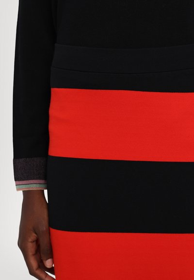 Robe rayée noire et rouge avec un haut noir ajusté et un bas présentant des rayures horizontales audacieuses rouges et noires. Les poignets sont ornés d'un accent multicolore.